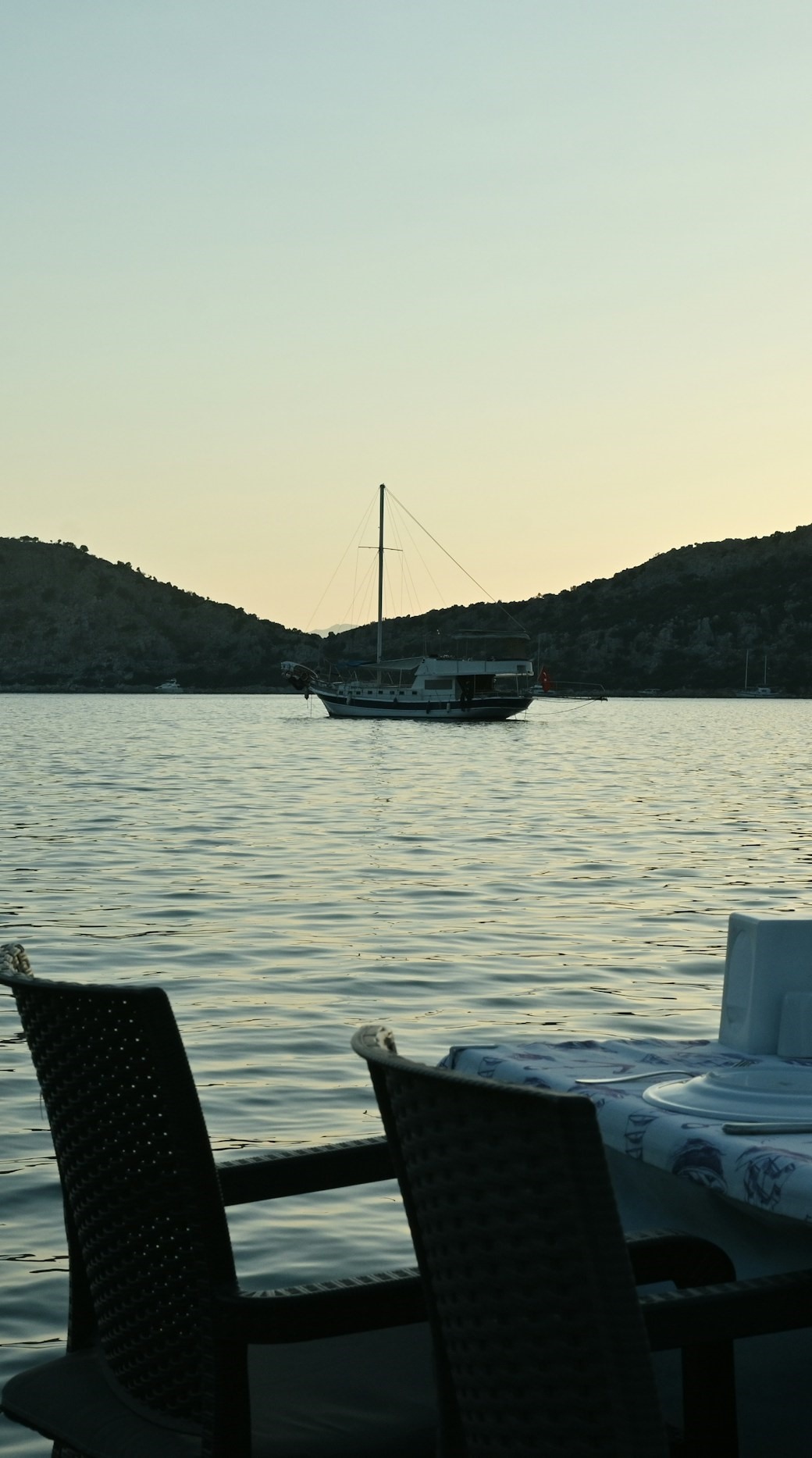 Στρωμένο τραπέζι σε deck πάνω από ήρεμο κόλπο στο σούρουπο (προσωρινή φωτογραφία)
